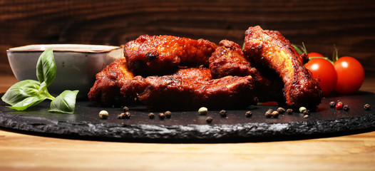 Spicy hot grilled spare ribs from a summer BBQ served with fresh tomatoes on an vintage cutting board