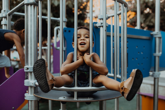 African American boy with funny face looking at camera while sitting behind grating on playground in park