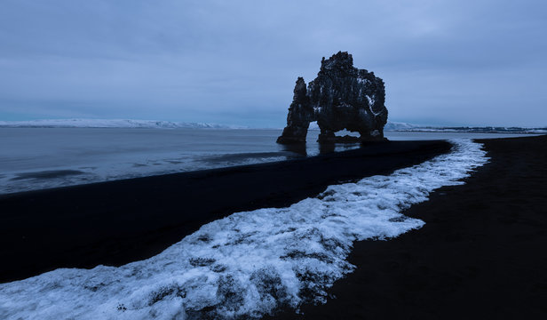 Picturesque view of pebble beach of seashore with rocks in water under gloomy sky in HvÌtserkur Iceland