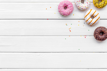 Fototapeta na wymiar Glazed decorated donuts for sweet break on white wooden background flat lay copy space