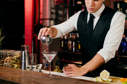 Crop anonymous young elegant barman working behind a bar counter mixing drinks with fruits