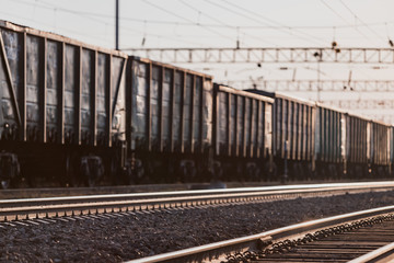 Obraz premium The train is on the railway track. Many cars with cargo in the rays of sunset lighting.
