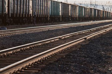 The train is on the railway track. Many cars with cargo in the rays of sunset lighting.