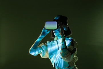 Excited young woman having virtual reality experience in neon light