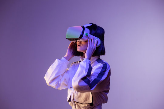 Excited young woman having virtual reality experience in neon light