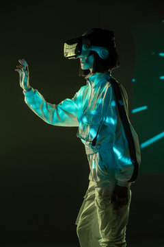 Excited young woman touching air while having virtual reality experience in neon light