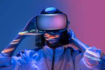 Excited young woman having virtual reality experience in neon light