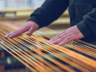 Anonymous worker touching orange cotton threads on weaver loom on factory
