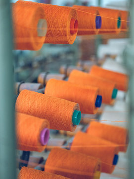 Spools with orange thread attached to industrial weaver loom on factory