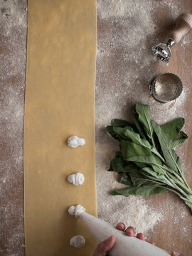 Hands of anonymous cook squeezing creamy filling on thin ravioli dough near bunch of fresh sorrel on table in kitchen