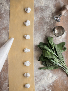 Hands of anonymous cook squeezing creamy filling on thin ravioli dough near bunch of fresh sorrel on table in kitchen