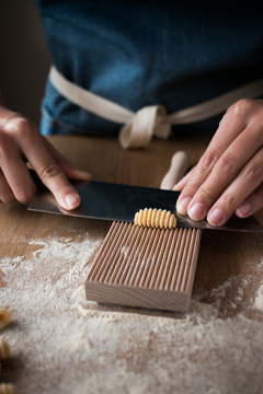 Anonymous female preparing dough for homemade gnocchetti pasta on a wooden tool in table in kitchen