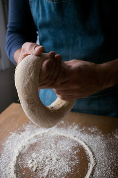 Unrecognizable cook shaping fresh dough with flour while cooking Rosca de Reyes over wooden table in kitchen