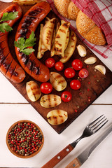 Fototapeta na wymiar Grilled sausages with vegetables, spices and bread on wooden cutting board background. Top view