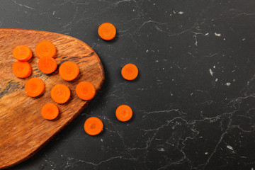 Tabletop view, carrot sliced to small circles on a chopping board, some on black marble next