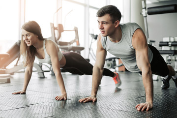 Sporty young couple doing plank exercise in gym