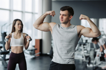 Fototapeta na wymiar Beautiful sports couple is showing their muscles while standing in gym
