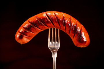 Extreme close-up Grilled sausage on a fork on a black background