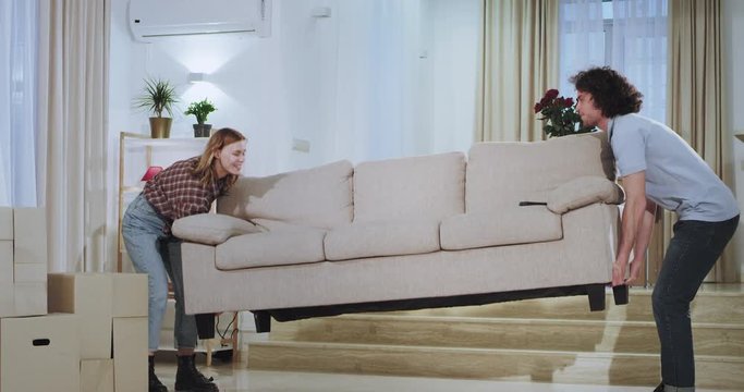 Attractive guy with his girlfriend moved in a new apartment they make some changes carrying the sofa in the middle of living room they excited take a sit on the sofa and start to watch the TV.