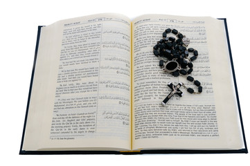 Catholic rosary beads sitting on top of an open Qu'ran.