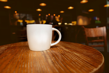 White Ceramic Coffee Cup On Wooden Table Against Dark Blurred Interior Of Coffee Shop.