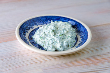 dinner sauce: sour cream and onions in a bright porcelain plate on a wooden table