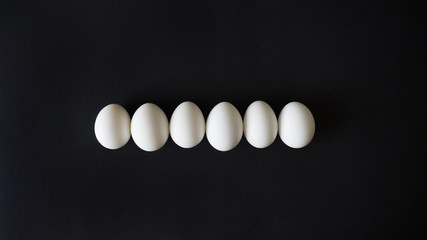 white chicken eggs lie exactly in line, ordered on a black isolated background, top view