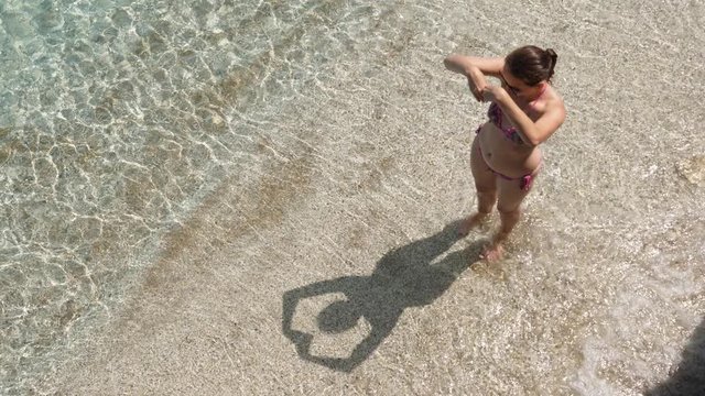 Woman play with shadow at sea beach, hold hands over head, trying to make heart shape on sand. Clear waters of sea wash her legs and picture on ground
