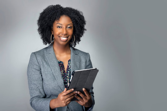 Black African American teacher or businesswoman sitting and holding a tablet computer.  The confident female author or writer looks like she is preparing for a seminar or as a keynote speaker.