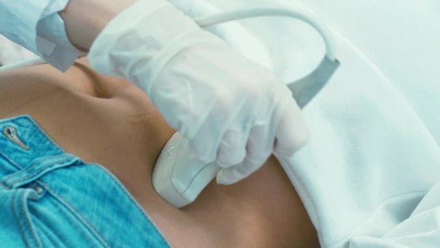 Close up shot of ultrasound scanner sliding on female abdomen