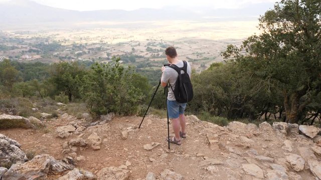 Tourist man take photo of Lasithi plateau, stay at top point with small camera on tripod. Hand held shot of traveller against famous Cretan landmark