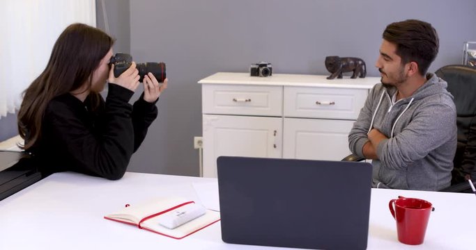 Young woman photographer working in a office taking photos of male model on digital camera