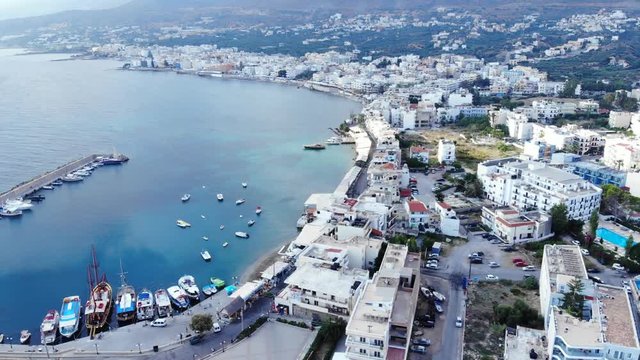 Quiet small Hersonissos town at North shore of Crete, aerial shot, camera fly back. Low rise hotel buildings and houses, little port, beach washed by crystal water