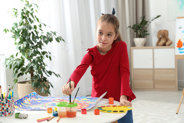 Little child painting picture at table indoors