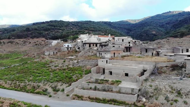 Aerial shot of forsaken village, empty broken houses begin destroyed with water flood. Sfendili settlement at reservoir of Aposelemis dam. Camera fly closer, dark gaps of empty windows