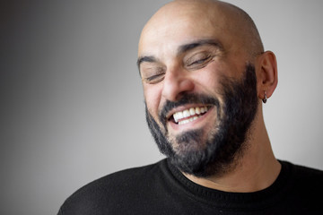 Close-up portrait of bearded bald man with earring and beautiful white teeth - obrazy, fototapety, plakaty