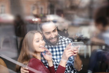 Lovely young couple spending time together in cafe, view from outdoors through window