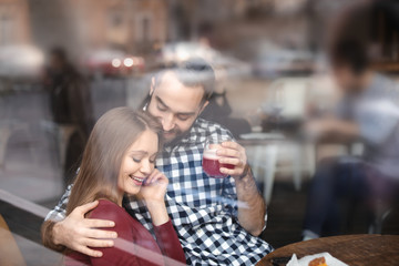 Lovely young couple spending time together in cafe, view from outdoors through window