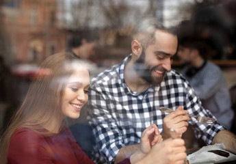 Lovely young couple spending time together in cafe, view from outdoors through window