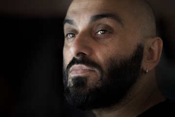 Close-up portrait of a bearded bald man with earring with black, dark background