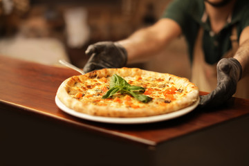 Man holding plate with oven baked pizza on table, closeup