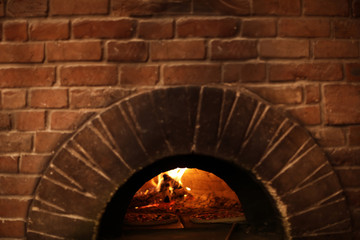 Brick oven with burning firewood and pizzas indoors