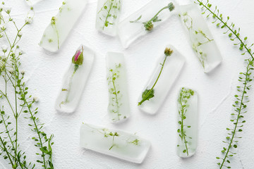Ice cubes with flowers on white background, flat lay