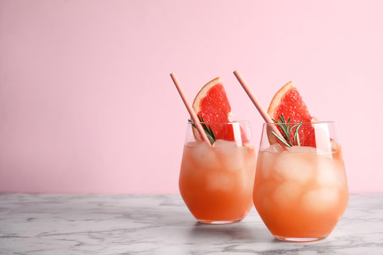 Glasses of grapefruit cocktails on table against color background. Space for text