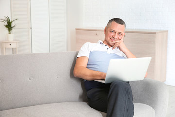 Mature man with laptop sitting on sofa at home
