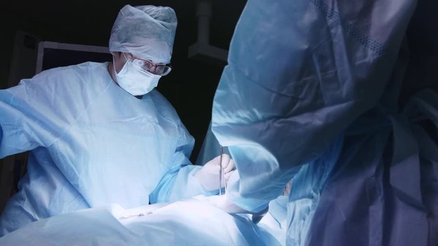Female doctor performing operation, taking surgical tools to stitch incision