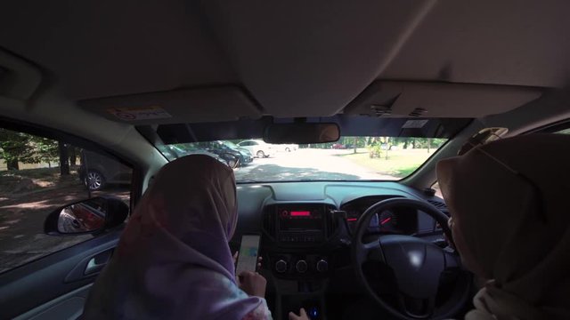 Two young Asian Muslim women in car, driving a car as pilot and as co pilot, pov from back seat inside the car. Co pilot using navigation map on the smartphone.