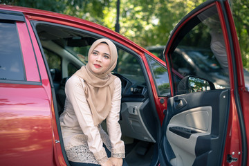 portrait of young muslim woman in hijab sitting on car seat with opened door. Female driver concept.