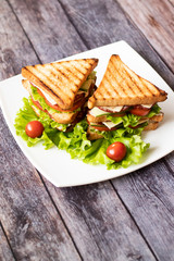 Sandwich with cheese, tomato, cucumber, sausage and lettuce on a wooden background. Vertical orientation