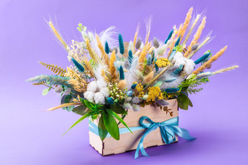 wooden box with beautiful spring flower bouquet decorated with feathers isolated on color background, close up